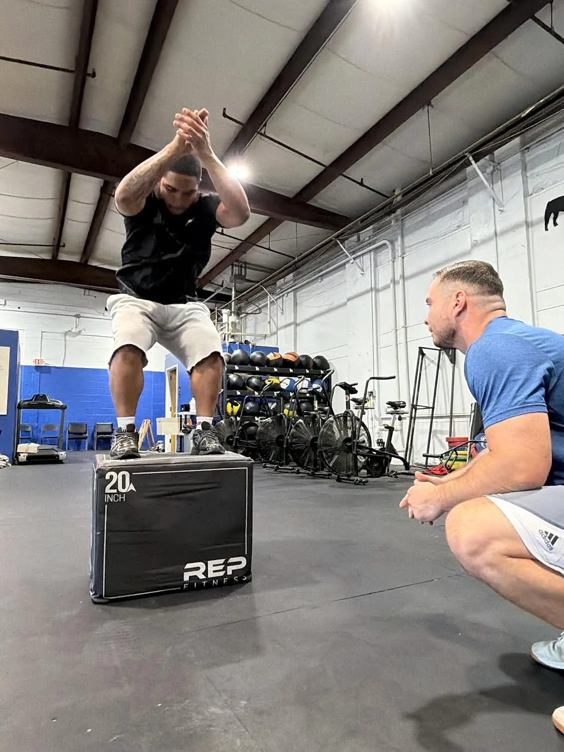 A client lands a box jump while Kyle watches from a crouch