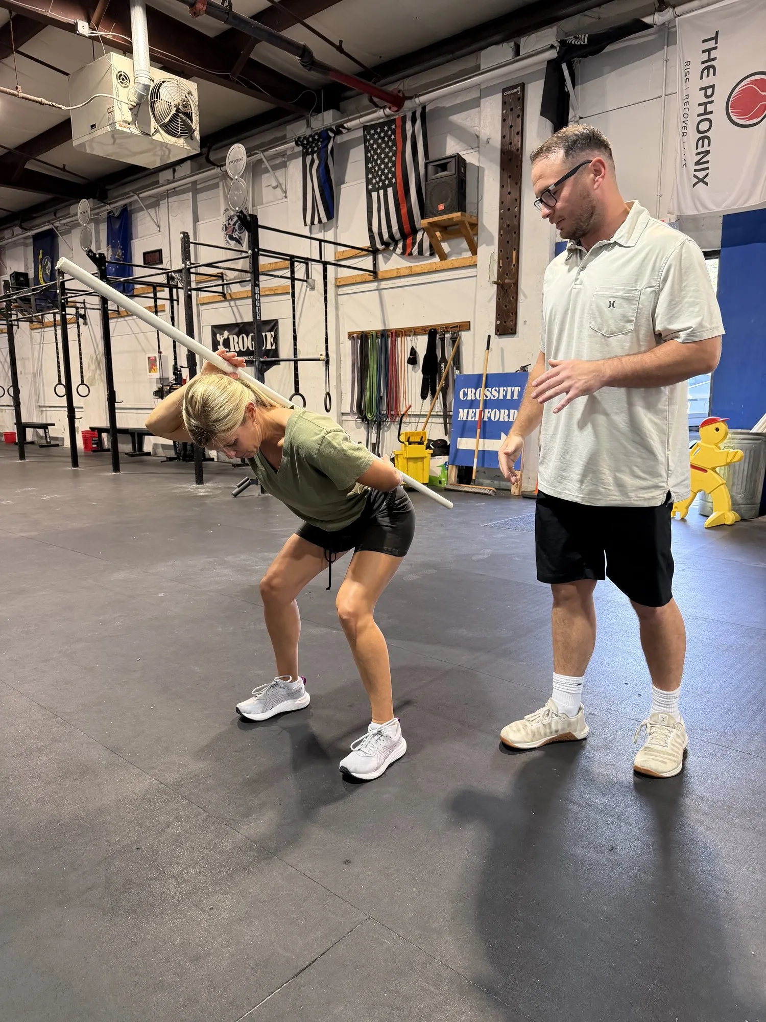 Kyle coaching a client through a hip hinge with a dowel along her back