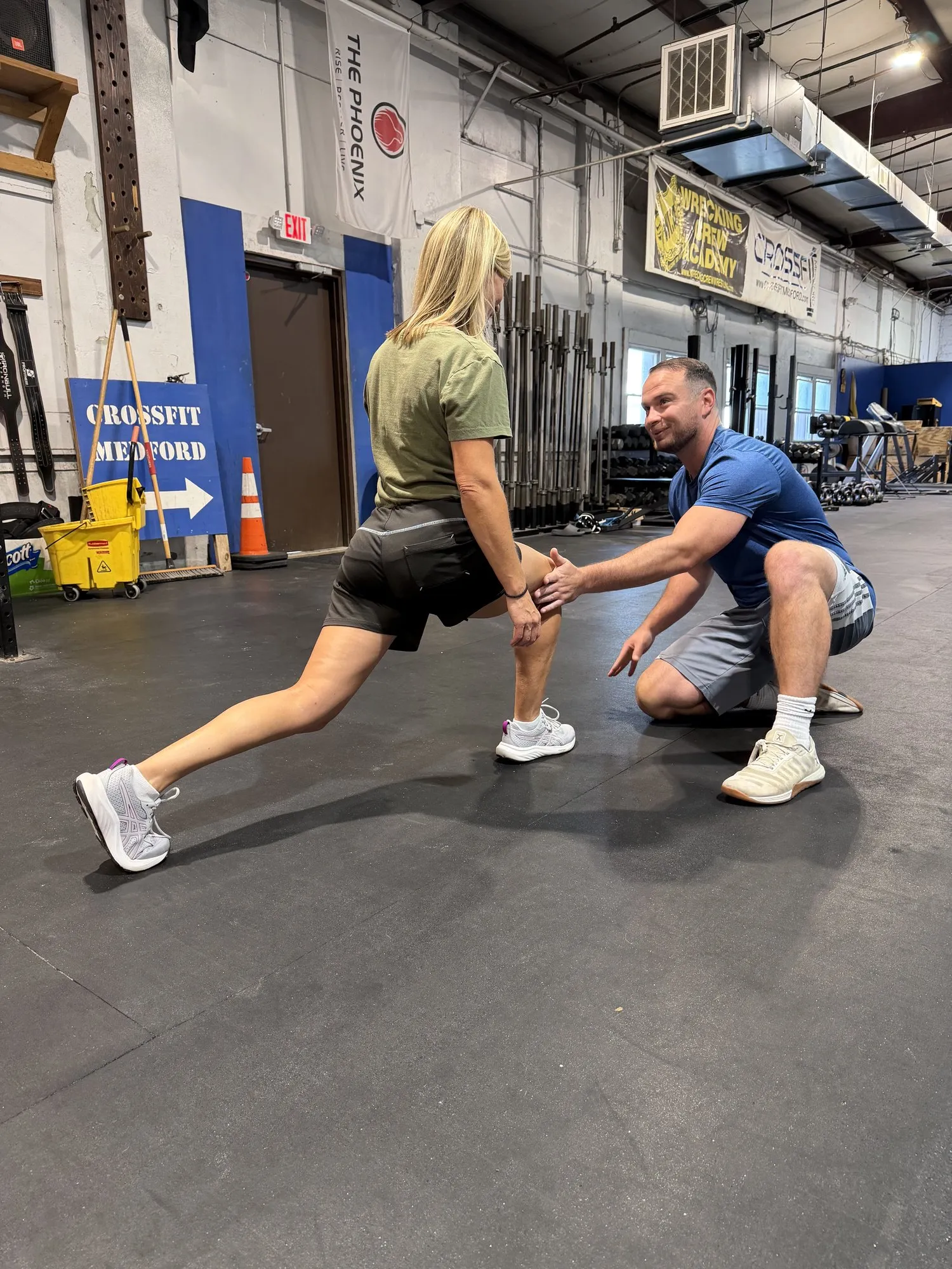 Kyle kneeling beside a client in a lunge, guiding her knee position